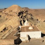 Guermassa Tataouine sud Tunisie est l'un des plus beaux villages-citadelles de la région du Dahar. Perché entre 450 et 500 mètres d'altitude, il se déroule sur 17 hectares sur la crête et la colline du Djebel Kedim. Guermassa est un village troglodytique parfaitement intégré dans son environnement naturel. Organisé en rangées de maisons troglodytiques latérales creusées entre les couches géologiques et utilisant les matériaux de leurs roches, il est en parfaite harmonie avec la morphologie et la géologie de la montagne qu'il occupe. Le village est riche de plusieurs composantes patrimoniales typiques du Dahar : un ksar citadelle à son sommet (dont il ne reste que des ruines) appelé galla, un ksar destiné au stockage des récoltes, une mosquée datée de 1860, une huilerie, des habitations troglodytiques en nombre et même une nécropole. A pied, le tour complet du village nécessite au moins une heure, et nous vous conseillons de réaliser cette visite !