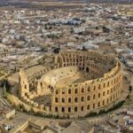 Une excursion à El Jem, également orthographié "El Djem", est une expérience incontournable pour les visiteurs en Tunisie, en particulier pour les passionnés d'histoire et d'architecture. El Jem est une petite ville située à environ 60 kilomètres au sud de Sousse et est célèbre pour son impressionnant amphithéâtre romain, l'un des sites les plus importants et les mieux conservés de l'ère romaine en Afrique du Nord. Voici ce que vous pouvez attendre lors d'une excursion à El Jem : Amphithéâtre romain d'El Jem : Le joyau d'El Jem est sans aucun doute son amphithéâtre, qui est souvent comparé au Colisée de Rome en Italie en raison de sa taille et de sa grandeur. Construit au IIIe siècle après J.-C., il pouvait accueillir jusqu'à 35 000 spectateurs. L'amphithéâtre est bien préservé, et vous pouvez monter dans les gradins pour obtenir une vue imprenable sur l'arène et les environs. Musée archéologique : À proximité de l'amphithéâtre, vous trouverez un petit musée archéologique qui abrite des artefacts romains découverts dans la région, notamment des sculptures, des mosaïques et des objets du quotidien de l'époque romaine. La Médina d'El Jem : En dehors de l'amphithéâtre, la ville d'El Jem possède également une charmante médina où vous pouvez vous promener dans des ruelles étroites et découvrir la vie quotidienne des habitants. Les bains romains : À côté de l'amphithéâtre, vous pouvez également visiter les vestiges des anciens bains romains, qui offrent un aperçu intéressant de la vie publique et sociale à l'époque romaine. La gastronomie tunisienne : Profitez de votre visite à El Jem pour déguster la délicieuse cuisine tunisienne dans l'un des restaurants locaux. Ne manquez pas de goûter aux spécialités locales, telles que le couscous, les tajines, les pâtisseries et les jus de fruits frais. Lors de votre excursion à El Jem, assurez-vous de porter des chaussures confortables, car vous passerez probablement du temps à explorer les ruines et à gravir les gradins de l'amphithéâtre. Si vous êtes passionné d'histoire, de culture romaine et d'archéologie, El Jem est une destination incontournable à ajouter à votre itinéraire en Tunisie.