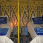 S’offrir deux jours et une nuit dans le Sahara tunisien, c’est faire une vraie coupure sans bloquer une semaine de vacances. En un week-end prolongé, nous vous emmenons au cœur des dunes, loin du bruit, pour une nuit magique sous les étoiles, des balades à dos de dromadaire, des repas typiques au feu de bois et des rencontres authentiques avec les habitants des oasis. Avec sudtunisie.com, ce mini-séjour est pensé comme une parenthèse intense : tout est organisé, de la navette aéroport à l’hébergement en bivouac, en passant par les transferts en 4×4 et les repas complets. Il ne vous reste qu’une chose à faire : vous laisser porter par le désert. Pour découvrir toutes nos options similaires, vous pouvez déjà jeter un œil à nos circuits désert en Tunisie . Pourquoi choisir un circuit Sahara “Deux jours, une nuit” en Tunisie ? Un circuit Sahara de deux jours et une nuit est idéal si vous voulez : Découvrir le désert sans y passer une semaine entière Combiner un séjour à Djerba, Tozeur, Douz ou Tataouine avec une immersion saharienne Vivre l’expérience d’un bivouac sous les étoiles, mais avec un confort maîtrisé Tester le désert avant, peut-être, de revenir plus longtemps En 48 heures bien remplies, vous avez le temps de : Traverser des paysages variés : chott salé, pistes sablonneuses, petites dunes, oasis Profiter d’une balade à dos de dromadaire au coucher du soleil Partager un dîner traditionnel autour du feu Dormir dans une tente saharienne ou un camp de charme Voir, au lever du jour, le premier soleil glisser sur les dunes Ce format court convient parfaitement : Aux familles avec enfants (rythme doux, activités ludiques) Aux couples en escapade romantique Aux amis qui cherchent une expérience forte pendant un séjour en Tunisie Aux voyageurs pressés qui veulent goûter au désert entre deux obligations Pour avoir une vue d’ensemble sur nos autres formules plus longues (3, 4, 5 jours et plus), consultez la page circuits désert sudtunisie.com . Jour 1 – Cap sur les dunes : pistes, chott et nuit au bivouac Prise en charge et transfert vers le désert Dès le matin, nous vous récupérons à votre hôtel ou directement à l’aéroport grâce à notre service de navette aéroport . Que vous arriviez à Tozeur, Djerba ou Gabès, nous adaptons l’itinéraire pour optimiser votre temps dans le désert. Une fois installés dans le 4×4, c’est le début de l’aventure. Votre chauffeur-accompagnateur vous explique le déroulé des deux jours, le type de terrain que vous allez traverser, et répond à vos questions. Nous aimons garder un ton convivial, sans discours compliqué : l’idée est que vous soyez à l’aise et que vous profitiez de chaque instant. Découverte des paysages sahariens : chott, pistes et premières dunes Selon votre point de départ, vous pouvez : Traverser le Chott El-Jérid, immense lac salé aux reflets irréels, parfait pour les photos Rejoindre les portes du désert vers Douz ou Ksar Ghilane par de longues lignes droites puis des pistes sablonneuses Croiser des palmeraies, des petites fermes oasiennes, des villages où le temps semble suspendu Nous faisons régulièrement des pauses panoramiques : photos, petites marches, explications sur la vie dans le désert, culture locale, traditions nomades. L’objectif n’est pas de “foncer”, mais de goûter au rythme du Sahara. Déjeuner nomade et arrivée au camp Vers midi, vous profitez d’un déjeuner simple et savoureux, soit en restaurant local, soit en pique-nique aménagé selon l’itinéraire. Nous privilégions les produits frais et les recettes locales : salades, plats chauds, fruits de saison, et bien sûr thé à la menthe. L’après-midi, les pistes vous mènent progressivement vers les dunes plus marquées. Quand la lumière commence à baisser, le 4×4 s’arrête enfin près de votre camp saharien ou bivouac privatif. Installation dans votre tente ou votre lodge : lits ou matelas confortables, couvertures suffisantes, possibilité de sanitaires partagés ou intégrés selon la catégorie choisie. Balade à dos de dromadaire au coucher du soleil Moment fort de la journée : la balade à dos de dromadaire. En file douce, accompagnés par des chameliers locaux, vous partez pour 30 à 60 minutes à travers les dunes. Le silence, le sable sous les pieds des dromadaires, le ciel qui change de couleur… C’est souvent ici que l’on ressent pour la première fois la vraie magie du Sahara. De retour au camp, l’appétit est là. Pendant que vous vous détendez, notre équipe prépare le dîner : soupe chaude, couscous, viandes grillées, légumes cuits doucement, dattes, fruits secs… L’ambiance est chaleureuse, parfois accompagné de musique traditionnelle. Nuit sous les étoiles : le cœur du circuit Sahara Après le repas, place à la contemplation. Loin des lumières de la ville, le ciel s’embrase d’étoiles. Échanges autour du feu, photos, silence total… Chacun vit ce moment à sa manière, mais une chose est sûre : on ne l’oublie pas. Vous rejoignez ensuite votre tente ou votre chambre, avec la sensation d’être au bout du monde, alors que vous n’êtes, en réalité, qu’à quelques heures de vol de l’Europe. Jour 2 – Lever de soleil, dunes et retour par les oasis Lever de soleil sur les dunes Le deuxième jour commence souvent tôt : ceux qui le souhaitent se lèvent pour assister au lever de soleil sur les dunes. L’air est frais, la lumière rose, le sable encore froid. C’est un moment privilégié pour faire quelques photos sans personne, ou simplement s’asseoir et observer le désert s’éveiller. Après le spectacle, retour au camp pour un petit-déjeuner copieux : café, thé, pain, crêpes, confitures, dattes, œufs… L’idée est de prendre des forces avant la suite du programme. Balade à pied ou en 4×4 dans les environs En fonction de votre niveau d’énergie, nous proposons : Une petite marche à pied dans les dunes proches, pour ressentir le sable, monter sur les crêtes, profiter des panoramas Une boucle en 4×4 autour du camp, avec arrêt dans des zones de dunes plus hautes ou plus isolées Parfois, l’approche d’un ancien fort, d’un petit village ou d’un point d’eau Ceux qui aiment marcher peuvent prolonger la découverte en mode randonnée, et pour les voyageurs plus sportifs, de plus longues randonnées en montagne saharienne sont possibles sur d’autres séjours : à ce sujet, nous proposons des programmes spécifiques de randonnée en montagne dans le Sahara . Oasis, artisanat et retour vers votre point de départ En fin de matinée, le camp est quitté. Nous reprenons la piste vers les oasis et les villages. Quelques haltes typiques : Visite d’une palmeraie et explication sur la culture des dattes Deglet Ennour Découverte d’un atelier d’artisanat (tressage, poterie, tissage) Pause café ou thé dans un petit café local En début d’après-midi, selon l’itinéraire, nous reprenons la route vers Douz, Tozeur, Tataouine ou Djerba, où vous pouvez : Récupérer vos bagages et continuer votre séjour Prendre un autre circuit ou une excursion en Tunisie Rejoindre l’aéroport via notre navette pour votre vol retour Départs possibles et exemples d’itinéraires 2 jours / 1 nuit Depuis Tozeur : chott, oasis et dunes Au départ de Tozeur, un circuit classique sur deux jours et une nuit peut inclure : Traversée du Chott El-Jérid Arrivée vers Douz ou une zone de dunes à proximité Bivouac ou camp saharien Retour par les oasis de montagne ou par une variation de piste selon le temps disponible C’est une excellente option si vous combinez votre mini-circuit avec la visite de Chebika, Tamerza ou Midès lors d’une autre excursion ou d’un voyage plus long. Depuis Djerba / Tataouine : ksour et Ksar Ghilane Au départ de Djerba ou Tataouine, nous aimons intégrer : Passage par un village berbère ou un ksar (ancien grenier fortifié) Route vers Ksar Ghilane, l’oasis au bord du désert Détente au bain thermal (selon saison et disponibilité) Bivouac ou camp dans les dunes environnantes Le lendemain, retour vers Djerba avec possibilité de petites escales panoramiques, ou de prolonger par une journée supplémentaire. Depuis Douz : immersion directe dans l’erg Si vous êtes déjà à Douz, porte du désert, le 4×4 quitte rapidement la ville pour plonger dans les dunes. Deux jours / une nuit permettent : De s’enfoncer suffisamment pour avoir le sentiment d’être vraiment en plein désert De profiter pleinement du coucher et du lever de soleil De revenir tranquillement, sans marathon, pour reprendre votre route Prestations incluses : ce que comprend votre excursion Sahara 2 jours / 1 nuit Sur ce type de circuit, nous incluons généralement : Prise en charge à l’hôtel ou à l’aéroport (via notre service de navette aéroport ) Véhicule 4×4 avec chauffeur-accompagnateur francophone (ou autre langue, selon disponibilité) Carburant, péages et frais de piste Une nuit en camp ou bivouac (catégorie selon votre choix) Dîner du jour 1, petit-déjeuner du jour 2 et souvent déjeuner (à confirmer dans le devis) Balade à dos de dromadaire (départ du camp) Assistance et encadrement durant tout le circuit Certaines options peuvent être ajoutées : quad, activités spécifiques, demandes particulières pour anniversaire, voyage de noces, team-building, etc. Pour des expériences plus sportives ou plus longues, nous proposons aussi des randonnées en montagne saharienne et des circuits trekking. Nos circuits désert détaillent toutes ces variantes. Pour qui est fait ce mini-circuit saharien ? Familles avec enfants Le format deux jours / une nuit est parfait pour un premier contact avec le désert : Étapes adaptées au rythme des enfants Animations simples : chameaux, jeu de traces dans le sable, observation des étoiles Distance raisonnable en 4×4 pour éviter la fatigue Couples en escapade romantique Rien de plus romantique qu’un coucher de soleil dans les dunes et une nuit loin des lumières. Sur demande, nous pouvons : Prévoir une tente privatisée à l’écart Aménager une petite surprise (gâteau, décoration simple, etc.) Conseiller de prolonger le séjour par une journée détente dans un lodge ou une oasis Groupes d’amis et voyageurs pressés Vous êtes en road-trip en Tunisie et n’avez que deux jours libres ? Ce mini-circuit vous offre un condensé de Sahara sans désorganiser tout votre planning. Pour des idées complémentaires d’itinéraires et d’excursions, consultez notre page excursion en Tunisie ainsi que notre blog d’excursions en Tunisie . Conseils pratiques pour profiter pleinement de 2 jours et 1 nuit dans le Sahara Prévoyez des vêtements en couches : T-shirt, polaire, coupe-vent. La journée peut être douce, la nuit plus fraîche. Portez des chaussures fermées confortables (baskets ou chaussures de marche). N’oubliez pas : lunettes de soleil, casquette ou chèche, crème solaire, petit sac à dos pour vos affaires de la journée. Pensez à une batterie externe pour vos appareils (dans le désert, les prises sont limitées). Hydratez-vous régulièrement, même si vous n’avez pas particulièrement soif. Pour plus de conseils, d’idées d’itinéraires et de retours d’expérience, nous mettons à jour notre blog d’excursions en Tunisie avec des articles pratiques et inspirants. Avis voyageurs et gage de sérieux : ce que disent ceux qui sont déjà partis Avant de réserver, il est normal de vouloir savoir à qui vous confiez votre voyage. Pour cela, rien de plus transparent que les avis clients. Vous pouvez lire les retours d’expérience sur Sud Tunisie directement sur TripAdvisor : 👉 Avis sur Sud Tunisie – Tozeur Ces avis reflètent notre manière de travailler : proximité, organisation sérieuse, respect du rythme de chaque voyageur et amour sincère du désert. Comment réserver votre circuit Sahara 2 jours / 1 nuit avec sudtunisie.com ? 1. Explorer les idées de circuits Commencez par parcourir nos circuits désert en Tunisie : vous y trouverez différents formats, au départ de plusieurs villes, avec des durées variées. Cela vous donne une base pour savoir ce qui vous plaît le plus : dunes, oasis, montagne, villages berbères… 2. Demander un devis personnalisé et gratuit Ensuite, envoyez-nous vos envies via notre formulaire dédié. En quelques minutes, vous pouvez demander un devis détaillé, sans engagement : 👉 Devis voyage désert – Tunisie Sahara Indiquez : Vos dates approximatives Le nombre de personnes (adultes, enfants) Votre ville de départ ou votre point d’arrivée en Tunisie Le type d’ambiance souhaitée (plutôt aventure ou plutôt confort/charme) Nous vous répondons avec une proposition sur mesure : itinéraire, hébergements, budget et options possibles. 3. Organiser les transferts et ajuster les détails Une fois le circuit validé, nous vous aidons à organiser : Les transferts aéroport via notre service de navette Les éventuelles excursions complémentaires (oasis de montagne, visites culturelles, randos) : Excursions en Tunisie Randonnée montagne Sahara Nous restons disponibles pour ajuster les horaires, répondre à vos questions pratiques et adapter le programme. FAQ – Excursion Sahara 2 jours / 1 nuit Est-ce suffisant pour “voir le désert” ? Oui, si l’objectif est de vivre une première immersion : dunes, coucher et lever de soleil, bivouac, dromadaire. Pour aller plus loin dans l’erg ou combiner plusieurs régions, il faudra envisager 3 à 5 jours ou plus. Peut-on partir avec des enfants ? Absolument. Nous adaptons les distances, les horaires et les activités. Nous vous conseillons juste de prévoir chapeau, crème solaire et vêtements confortables. Quid du confort au bivouac ? Selon la formule choisie, vous dormez en tente équipée ou en camp aménagé. Les détails (sanitaires, literie, chauffage) sont précisés dans votre devis. Est-il possible de privatiser le circuit ? Oui, nous proposons aussi des circuits privés pour couples, familles ou groupes d’amis. Il suffit de le préciser dans votre demande de devis . Prêts pour deux jours et une nuit au cœur du Sahara tunisien ? En deux jours et une nuit, vous pouvez : Traverser des décors sahariens spectaculaires Vivre un coucher de soleil inoubliable dans les dunes Partager un dîner traditionnel sous un ciel chargé d’étoiles Dormir en bivouac ou camp saharien Revenir avec cette sensation rare d’avoir coupé avec le quotidien, même sur un court séjour Pour construire votre mini-séjour dans le désert, explorez nos circuits désert , puisez des idées sur notre blog d’excursions en Tunisie , puis envoyez-nous votre demande de devis gratuit . Avec sudtunisie.com, votre circuit et excursion Sahara en Tunisie – deux jours, une nuitée devient une expérience intense, accessible et parfaitement encadrée, que vous voyagiez en famille, en couple, entre amis ou en solo.