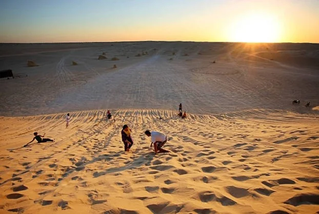 Le Sud tunisien nous appelle par ses dunes blondes, ses oasis suspendues, ses ksour ancestraux et ses villages troglodytiques qui racontent des siècles d’ingéniosité. Nous concevons des circuits désert et des excursions au jour le jour, taillés pour ceux qui veulent goûter l’essentiel du Sahara sans renoncer au confort ni aux rencontres authentiques. Avec nous, votre aventure démarre depuis l’adresse de votre choix en Tunisie (hôtel, aéroport, domicile, gare), et se façonne sur mesure : 2 jours/1 nuit, 3, 5, 7 ou 8 jours… ou plus, si vous voulez prolonger le plaisir. Circuits désert en Tunisie : nos itinéraires phares à personnaliser Avant tout, explorez notre sélection complète de programmes sur Circuits Désert Sahara . Vous y trouverez des canevas testés sur le terrain, prêts à affiner, à adapter, à étendre ou à développer selon votre rythme et vos envies. 2 jours / 1 nuit – Immersion express Douz – Ksar Ghilane (bivouac au choix) Jour 1 : Accueil à Douz, la “porte du désert”. Cap en 4×4 sur les dunes de l’Erg oriental. Pause thé, marche légère sur les crêtes au coucher du soleil, installation du bivouac nomade ou du camp confort. Jour 2 : Piste vers Ksar Ghilane, baignade possible dans la source chaude, sieste à l’ombre des tamaris, déjeuner à la campement puis retour. Pour qui ? Voyageurs pressés qui veulent le goût du Sahara et une nuit sous les étoiles, sans logistique lourde. 4 jours / 3 nuits – Chott el-Jérid, Ong Jmel, oasis de montagne et troglodytes Jour 1 : Tozeur – vieille ville en briques, palmeraie en calèche ou à vélo. Jour 2 : Ong Jmel et ses dunes cinématographiques, traversée du Chott el-Jérid (arrêts photo sur les mirages), nuit à Douz. Jour 3 : Bivouac dans l’Erg : dîner sous la Voie lactée, pain cuit sous le sable. Jour 4 : Chebika – Tamerza – Mides, sentiers au fil de l’eau, canyons et panoramas, retour à Tozeur. Pour qui ? Ceux qui veulent désert + salin + oasis en un compact équilibré. 7–8 jours – La grande traversée : Douz, Ksar Ghilane, Tataouine, ksour & Matmata Jours 1–2 : Tozeur, Chott el-Jérid, Douz et mise en jambe saharienne. Jour 3 : Nuit en plein désert, silence minéral, ciel constellé. Jour 4 : Ksar Ghilane : baignade, fort romain, dunes souples. Jour 5 : Cap sur Tataouine et les ksour, coucher de soleil à Chenini. Jour 6 : Ksar Ouled Soltane, greniers superposés, balade artisanale. Jour 7 : Matmata et l’architecture troglodytique. Jour 8 : Transfert flexible (Tozeur, Djerba, Tunis) selon vos vols. Pour qui ? Les voyageurs qui veulent prendre le temps, multiplier les ambiances et rencontrer les gens. Tous ces itinéraires servent de base modulable : nous ajustons les distances, le niveau de confort, le nombre de nuits en bivouac, et même les parenthèses thématiques (photo, gastronomie, géologie, traditions). Découvrez, comparez, et revenez vers nous avec vos priorités pour que nous mettions tout cela à développer ensemble sur cette page . Excursions au Sud tunisien : une journée, un concentré d’émerveillement Vous avez peu de temps ? Une excursion bien pensée suffit pour capter l’essence du Sud. Composez votre panier d’incontournables sur Excursion en Tunisie et puisez des idées fraîches sur notre blog d’excursions . Oasis de montagne : Chebika – Tamerza – Mides Entre sources claires, palmeraies accrochées et canyons striés, ce trio régale l’œil et l’objectif. Marche facile, baignade de cheville, pause citronnade. Départ idéal depuis Tozeur. Ong Jmel & décors du désert À quelques dunes de Tozeur, on s’amuse en 4×4, on grimpe pour le panorama, on capture le sable qui ondule. Demi-journée ludique et photogénique. Troglodytes de Matmata & village perché de Tamezret Au départ de Djerba ou Gabès, on plonge dans la vie souterraine des maisons creusées. Rencontre avec les habitants, découverte du pain tabouna et de l’huile d’olive locale. Douz, dromadaires & coucher de soleil Quand le temps manque, l’or du soir autour de Douz suffit pour graver la mémoire : balade chamelière, dîner traditionnel… et ce silence qui impressionne toujours la première fois. Randonnée & trekking : crêtes, ergs et nuits étoilées Pour ceux qui aiment avancer à pied et compter le temps autrement, nous dessinons des boucles sur mesure, de la balade familiale au trek soutenu, mêlant crêtes rocheuses, oueds, plateaux tabulaires et dunes. Consultez nos inspirations et niveaux conseillés sur Randonnée Montagne & Sahara (et gardez le lien, nous y ajoutons régulièrement des variantes : randonnée montagne & Sahara ). Exemple de journée rando “signature” Aube : lumière dorée sur l’erg, départ frais. Matin : arêtes panoramiques, lecture du paysage (vent, strates, végétation). Midi : pique-nique à l’ombre d’un tamaris, sieste courte. Après-midi : descente douce vers l’oued, pas dans le sable, souffle régulier. Soir : campement, ciel profond, contes nomades et pain sous la cendre. Prise en charge partout en Tunisie : navettes et transferts fluides Nous venons vous chercher là où vous êtes : à Tunis, Hammamet, Sousse, Monastir, Sfax, Djerba, Tozeur, Gabès… ou devant votre porte si vous résidez en Tunisie. Gagnez un temps précieux avec notre service de navette aéroport : voiture ou minibus récents, chauffeurs expérimentés, coordination directe avec vos vols, arrivée sans stress au point de départ du circuit. Logistique & confort : hébergements, bivouacs, sécurité Dormir dans le désert… à votre façon Bivouac nomade : tentes sahariennes, feu de camp, magie brute du ciel nocturne. Camp confort : lits, sanitaires, douches chaudes, électricité le soir. Maisons d’hôtes & hôtels : charme, proximité des sites, accueil familial. Manger bon, local et adapté Nos repas respectent vos régimes (végétarien, sans gluten, allergies – à nous signaler). Au menu : couscous, méchoui, chakchouka, ojja, salades de saison, dattes Deglet Nour. Sécurité & sérénité Avant chaque départ, briefing sur l’étape, hydratation, météo et rythme. Sur certaines boucles isolées : téléphone satellite, radio et points d’eau balisés. Notre règle d’or : l’expérience avant la performance. Circuits personnalisés 100 % sur mesure : 2j/1n… ou plus Votre planning n’est pas standard ? Parfait : nous adorons adapter. Week-end d’évasion : 2 jours/1 nuit avec coucher de soleil sur l’erg et bivouac. Mini-croisière saharienne : 3–4 jours, dunes + oasis de montagne. Grande traversée : 7–10 jours, ajout des ksour, troglodytes et plages de Djerba en fin de parcours. Thèmes : photo, géologie, artisanat, cuisine, bien-être, itinérance douce avec dromadaires de bât. Point de départ flexible : depuis l’adresse que vous voulez en Tunisie, nous organisons le ramassage, la logistique 4×4, et le calendrier d’étapes qui colle à vos vols. Conseils pratiques : quoi emporter, quand venir, comment s’habiller Saison : d’octobre à avril, le désert est idéal (doux le jour, frais la nuit). En mai/sep., départs tôt et fins d’après-midi privilégiés. L’été, programmes courts et campements climatisés. Sac : préférez un sac souple, plus simple dans les 4×4 et au camp. Indispensables : chèche/casquette, lunettes UV, crème solaire, gourde, coupe-vent léger, lampe frontale, chaussures fermées confortables. Photo : batteries de rechange, housse anti-sable, chiffon microfibre. Respect : on laisse zéro trace ; on photographie les personnes avec leur accord. Réserver simplement : devis gratuit, réponses rapides, ajustements illimités Dites-nous : vos dates, votre ville de départ en Tunisie, votre niveau de confort (bivouac rustique ou camp confort), vos envies (marche, culture, couchers de soleil, observation des étoiles, photographie). Nous revenons vers vous avec une proposition claire, modulable à l’infini jusqu’à ce qu’elle vous ressemble. Lancez votre projet ici : devis voyage désert – gratuit . Explorez nos circuits désert pour préciser vos préférences. Inspirez-vous côté excursions en Tunisie et côté blog excursions pour les idées du moment. Les marcheurs ? Cap sur randonnée montagne & Sahara pour choisir votre niveau. Ce que nos voyageurs apprécient le plus La liberté : départ depuis l’adresse de votre choix et rythme à votre mesure. La variété : en quelques jours, on passe du salar rose aux gorges verdoyantes et à la mer de sable. Le confort : hébergements choisis, véhicules récents, navettes aéroport sans couture. L’humain : artisans, familles troglodytes, gardiens de ksour, palmiculteurs… Des échanges simples, respectueux et mémorables. La transparence : un devis clair, des options posées, pas de surprises. Après votre retour, votre parole compte : laissez votre avis et partagez vos plus belles images sur notre page TripAdvisor . Vos retours inspirent les prochains voyageurs et nous poussent à faire toujours mieux. Idées d’itinéraires “à développer” ensemble Escapade 2j/1n – Départ depuis votre adresse en Tunisie Jour 1 : prise en charge à Tunis/Sousse/Monastir/Sfax/Djerba/Tozeur (ou autre), arrivée Douz, dunes au crépuscule, dîner sous les étoiles, bivouac. Jour 2 : Ksar Ghilane, source chaude, déjeuner traditionnel, retour – ou extension d’une nuit supplémentaire selon l’humeur. Signature 5j – Désert, salin & oasis Tozeur (vieille ville, palmeraie), Ong Jmel, Chott el-Jérid, Douz, bivouac, Chebika–Tamerza–Mides, transfert vers votre prochaine étape. Ajouts possibles : Matmata, Chenini, Ksar Ouled Soltane suivant vos envies. Grand tour 8j – Ksour & troglodytes en plus Douz – Ksar Ghilane – Tataouine – Chenini – Ksar Ouled Soltane – Matmata + options rando (voir randonnée montagne & Sahara ) pour pimenter certaines étapes. Pour chaque version, nous adaptons kilométrage, intensité des marches, nombre d’heures en 4×4, et niveaux d’hébergements. Votre sud tunisien doit être unique. Prêt pour l’aventure ? On s’occupe du reste Qu’il s’agisse d’une parenthèse de deux jours ou d’un périple d’une semaine, nous orchestrons transferts, hébergements, bivouacs, repas, autorisations et tous ces petits détails invisibles qui rendent un voyage fluide. Vous, vous profitez : lumières changeantes, silence habité, rencontres et cuisine du soleil. Démarrez maintenant avec un devis gratuit , puis continuez l’exploration sur circuits désert . Si vous arrivez par avion, pensez au service de navette aéroport . Et pour piocher des idées fraîches, passez par excursions en Tunisie et notre blog d’excursions . Rendez-vous dans le désert. Le soleil se couche, la dune rougit : votre histoire commence.