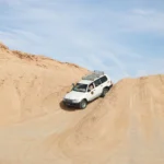 Bienvenue dans le Sud tunisien, terre de contrastes où l’ocre des dunes rencontre le vert tendre des oasis. Pour un réveillon inoubliable, nous proposons des circuits 100 % privés et des excursions sur mesure au cœur du Sahara tunisien. Entre Tozeur, Douz, Ksar Ghilane, Tamerza et Matmata, chaque étape a été pensée pour mêler paysages iconiques, authenticité et confort. Découvrez ci-dessous nos itinéraires phares, nos services inclus (dont la navette aéroport), nos conseils pratiques, et comment réserver votre devis gratuit en quelques clics. Pour parcourir nos programmes détaillés, consultez nos circuits dans le désert (lien à développer : https://sudtunisie.com/voyage/circuits-desert ). Pourquoi choisir le Sud tunisien pour votre fin d’année ? Le Sud est la promesse d’une parenthèse hors du temps : couchers de soleil flamboyants sur les dunes de Douz, dîners sous les étoiles, nuitées en camp confortable ou en tentes bédouines avec salle d’eau privée, et oasis de montagne aux cascades limpides. En décembre et janvier, les températures sont douces en journée, idéales pour la randonnée et les balades à dos de dromadaire. Loin des foules, on savoure le silence du Sahara, on partage un thé à la menthe au coin du feu, et on accueille la nouvelle année au rythme des percussions sahariennes. Authenticité garantie : villages troglodytiques, ksour (greniers fortifiés), marchés locaux, et accueil chaleureux. Confort et logistique maîtrisés : transferts fluides grâce à notre service de navette aéroport , hôtels sélectionnés, guides locaux francophones. Privatisation : chaque circuit sud Tunisie est adapté à votre rythme (familles, couples, petits groupes d’amis). Nos circuits désert (3 à 8 jours) : Tozeur, Douz, Matmata, Ksar Ghilane Nos circuits dans le désert sont modulables. Voici trois trames populaires, personnalisables selon vos envies. Circuit 3–4 jours : premiers pas dans le Sahara Jour 1 – Tozeur & Chott el-Jérid : accueil, transfert, palmeraies et médina. Coucher de soleil sur le Chott el-Jérid, le plus grand lac salé de Tunisie, célèbre pour ses miroirs de lumière. Jour 2 – Oasis de montagne : Chebika, Tamerza, Mides : canyons, cascades et panoramas grandioses. Jour 3 – Ong Jemel & désert : piste vers Ong Jemel (sites cinématographiques), balade à dos de dromadaire, bivouac sous les étoiles ou nuit en camp confort. Option Jour 4 : matinée libre dans les dunes, retour via Douz (souks de cuir, chéchias, dattes Deglet Nour). Idéal si vous cherchez un avant-goût du Sahara sans trop de route, avec hébergements cosy et activités emblématiques. Circuit 5–6 jours : grandes dunes & nuit en camp à Ksar Ghilane Jour 1 – Tozeur : accueil et immersion oasis. Jour 2 – Chebika/Tamerza/Mides : randonnées faciles, vues spectaculaires. Jour 3 – Douz & erg : traversée du Chott, arrivée aux grandes dunes de Douz, coucher de soleil inoubliable. Jour 4 – Ksar Ghilane : piste vers l’oasis saharienne et sa source chaude, détente et nuit en camp premium. Jour 5 – Matmata : découverte des maisons troglodytes, déjeuner traditionnel, moment photo dans les paysages lunaires. Jour 6 – Djerba ou Tozeur : selon vos vols, retour et temps libre pour un dernier café épicé. À retenir : plus de temps dans le désert, nuit magique à Ksar Ghilane, idéal pour un réveillon avec dîner local, musique bédouine et ciel constellé. Circuit 7–8 jours : le grand tour privé du Sud tunisien Tozeur, oasis de montagne, Douz, Ksar Ghilane, Matmata, Tataouine et ses ksour (Chenini, Guermessa), Djerba (option plage et patrimoine), puis retour. Activités : randonnées douces dans les canyons, dromadaires, 4×4 sur pistes, cuisine au feu de bois, ateliers artisanaux (poterie, tissage). Réveillon : dîner aux bougies, contes du désert, danse et percussions, coupe de thé au pignon pour fêter minuit. Ce format long permet de ralentir, de rencontrer et de s’imprégner. Parfait pour une Fête de la fin d’année en Tunisie mémorable. Retrouvez tous les programmes détaillés et options de personnalisation sur nos circuits désert . Excursion Sahara Tunisie : les incontournables à la journée Pas le temps pour un long séjour ? Nos excursions en Tunisie s’adaptent à votre agenda : Oasis de montagne (Chebika–Tamerza–Mides) : canyons, palmeraies suspendues, ponts naturels. Ong Jemel & désert de Tozeur : pistes de cinéma, balade chamelière, thé dans les dunes. Douz & mer de sable : coucher de soleil et soirée nomade légère. Ksar Ghilane : baignade dans la source chaude, fort romain au sommet des dunes, déjeuner méchoui. Chaque excursion Sahara Tunisie est privée, avec départ à l’heure qui vous convient, guide dédié et itinéraire modulable. Randonnée et trek dans le Sahara : du pas tranquille au défi doux Pour les amoureux de marche, nous avons conçu des itinéraires progressifs, de la balade facile au petit trek. Consultez la page Randonnée Montagne & Sahara pour des idées de boucles à la demi-journée, journées complètes ou 2 jours avec bivouac. Vous profitez de dénivelés raisonnables, de pauses photo et d’un pique-nique nomade face aux dunes. En hiver, les températures sont agréables pour marcher, et la lumière sublime les reliefs. Réveillon privé : dîner sous les étoiles, feu de camp et musique bédouine La Fête de fin d’année dans le désert n’a pas d’équivalent : Dîner saharien (soupe chorba, salades méchouia, couscous ou méchoui, fruits secs), pain cuit sous le sable (méthode traditionnelle), douceurs au miel. Musique et contes : percussionnistes, chansons du désert, danses légères. Ciel profond : loin des villes, la Voie lactée apparaît souvent à l’œil nu. Minuit : moment de partage, surprise gourmande et photos souvenirs. Nous privatisons l’espace de fête pour votre famille ou votre groupe, afin de préserver intimité et sécurité. Hébergements & camps : charme, confort et authenticité Selon le niveau de confort souhaité, nous sélectionnons : Maisons d’hôtes dans les oasis (charme, table locale). Hôtels 3★ à 5★ à Tozeur, Douz ou Djerba. Camps dans le désert : tentes spacieuses, literie confortable, sanitaires privés ou partagés. Bivouac premium : site isolé, service attentif, dîner au feu de bois. Tous les hébergements sont visités et contrôlés régulièrement pour garantir qualité et sécurité. Services inclus & options : tout pour un séjour fluide Transferts : navette aéroport (Tozeur, Djerba, Tozeur–Nefta), accueil à l’arrivée, transferts inter-étapes. Guides locaux francophones : passionnés, pédagogues, attentifs aux familles. Repas : selon programme (pique-niques, dîners, dégustations). Activités : dromadaires, 4×4, randonnée, ateliers artisanaux (en option). Assistance : support 7j/7, adaptation météo, aménagements pour enfants. Conseils pratiques : quand partir, quoi emporter, à qui s’adresse le voyage ? Période : de novembre à mars, la lumière est douce ; idéal pour un réveillon ou des vacances d’hiver. Tenue : superpositions (t-shirt, polaire, coupe-vent), écharpe pour la brise du soir, bonnes chaussures fermées, lunettes de soleil. Santé & sécurité : guides formés, itinéraires maîtrisés, eau embouteillée, cuisine soignée. Familles : nos circuits privés permettent siestes, pauses jeux et repas adaptés. Accessibilité : nous étudions les adaptations possibles (rythme, véhicule, chambre). Bagages : sacs souples de préférence, chargeur externe, lampe frontale, foulard pour le sable. Itinéraires thématiques : culture, nature, bien-être Culture & troglodytes : Matmata, Tataouine, ksour (Chenini, Ksar Ouled Soltane). Nature & oasis : Chebika–Tamerza–Mides, palmeraies de Tozeur, sources chaudes de Ksar Ghilane. Cinéma & paysages : Ong Jemel, Chott el-Jérid, plateaux mythiques et panoramas de sable infini. Bien-être : massages traditionnels (sur demande), bains chauds, yoga au lever du soleil (option). Pour vous inspirer, parcourez notre blog d’excursions en Tunisie : récits de voyage, idées d’itinéraires et conseils d’experts. Avis voyageurs : un gage de confiance La satisfaction de nos voyageurs est notre meilleure carte de visite. Consultez les retours et commentaires sur Tripadvisor : Sud Tunisie – Avis et expériences . Vous y trouverez des témoignages détaillés, des photos authentiques et des conseils partagés par ceux qui ont déjà vécu l’expérience. Devis gratuit, simple et rapide Vous avez une idée précise ou souhaitez un conseil personnalisé ? Demandez votre devis gratuit : Page devis : Demander un devis – Désert Sud Tunisie Lien contact direct : Devis voyage désert Sud Tunisie Expliquez-nous vos dates, votre budget, le confort souhaité, et les activités rêvées : nous vous répondons avec une proposition claire, détaillant étapes, hébergements, services et options. FAQ – Circuit Sud Tunisie & Excursion Sahara Tunisie — Combien de jours pour un premier désert ? 3 à 4 jours suffisent pour goûter aux dunes de Douz, voir le Chott el-Jérid et randonner dans une oasis de montagne. Pour Ksar Ghilane et les ksour, comptez 5 à 6 jours. Le grand tour se savoure en 7 à 8 jours. — Peut-on fêter le réveillon dans le désert ? Oui, nous organisons un réveillon privé avec dîner traditionnel, musique, et nuit en camp. Le tout en sécurité, encadré par nos équipes. — Et si nous voyageons avec des enfants ? Nous adaptons rythme, trajets et repas. Les dromadaires et les dunes sont souvent leur moment préféré ! — Quid des transferts aéroport ? Notre service de navette aéroport assure vos arrivées/départs à Tozeur, Djerba ou Gabès selon le circuit retenu. — Y a-t-il de la marche ? Oui, mais elle est souple et modulable. Pour des envies actives, explorez nos idées Randonnée Montagne & Sahara . — Comment réserver ? Choisissez un itinéraire sur Circuits désert , ou inspirez-vous via Excursion en Tunisie , puis envoyez-nous une demande via le devis gratuit . Nos engagements qualité : sécurité, clarté, personnalisation Sécurité : guides expérimentés, véhicules récents, itinéraires validés, suivi météo. Clarté : programmes détaillés, prestations précisées, pas de surprises. Personnalisation : privé de bout en bout, horaires flexibles, options à la carte (bien-être, ateliers, activités sportives). Impact local : partenariats avec artisans et maisons d’hôtes, contribution à l’économie du Sud tunisien. Idées d’itinéraires express pour la fin d’année (exemples privatisés) Réveillon 3 jours – Tozeur & dunes Jour 1 : Tozeur, palmeraies, coucher de soleil sur le Chott el-Jérid. Jour 2 : Chebika–Tamerza, puis Ong Jemel, soirée nomade sous les étoiles. Jour 3 : balade en dromadaire, déjeuner local, départ. Réveillon 5 jours – Grandes dunes & Ksar Ghilane Jour 1 : Tozeur, médina, artisanat. Jour 2 : oasis de montagne, randonnée douce. Jour 3 : Douz, mer de dunes, coucher de soleil. Jour 4 : Ksar Ghilane : source chaude, camp premium, dîner de réveillon. Jour 5 : Matmata troglodytique, route retour. Réveillon 7 jours – Grand tour culturel Jour 1–2 : Tozeur, oasis, Chott. Jour 3–4 : Douz, dunes, bivouac. Jour 5 : Ksar Ghilane, détente, feu de camp. Jour 6–7 : Matmata, ksour de Tataouine, Djerba (option plage & patrimoine). Ressources utiles pour préparer votre voyage Inspiration & récits : Blog – Excursions Tunisie Excursions à la carte : Excursion en Tunisie Trek & marche : Randonnée Montagne & Sahara Navettes & transferts : Services navette aéroport Programmes complets : Circuits désert (lien à développer : https://sudtunisie.com/voyage/circuits-desert ) Prêt à vivre votre Circuit Sud Tunisie ? Que vous rêviez d’un bivouac intimiste, d’un camp de charme ou d’un grand tour culturel, nous créons le voyage qui vous ressemble. Pour une Excursion Sahara Tunisie en famille, un réveillon privé entre amis ou une fugue romantique sous la Voie lactée, nous vous accompagnons pas à pas, avec le sourire et la rigueur qui font notre réputation. Explorez nos circuits dans le désert Choisissez vos excursions Découvrez nos randonnées montagne & Sahara Réservez vos navettes aéroport Demandez un devis gratuit Et pour partager votre expérience, laissez votre avis sur Tripadvisor – Sud Tunisie . Nous sommes impatients de vous accueillir, de Tozeur à Ksar Ghilane, pour célébrer la fin d’année en Tunisie comme vous ne l’avez jamais imaginée.